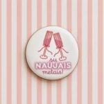 Supakuotas apvalus meduolis su šampano taurėmis ir užrašu „Su Naujais metais“